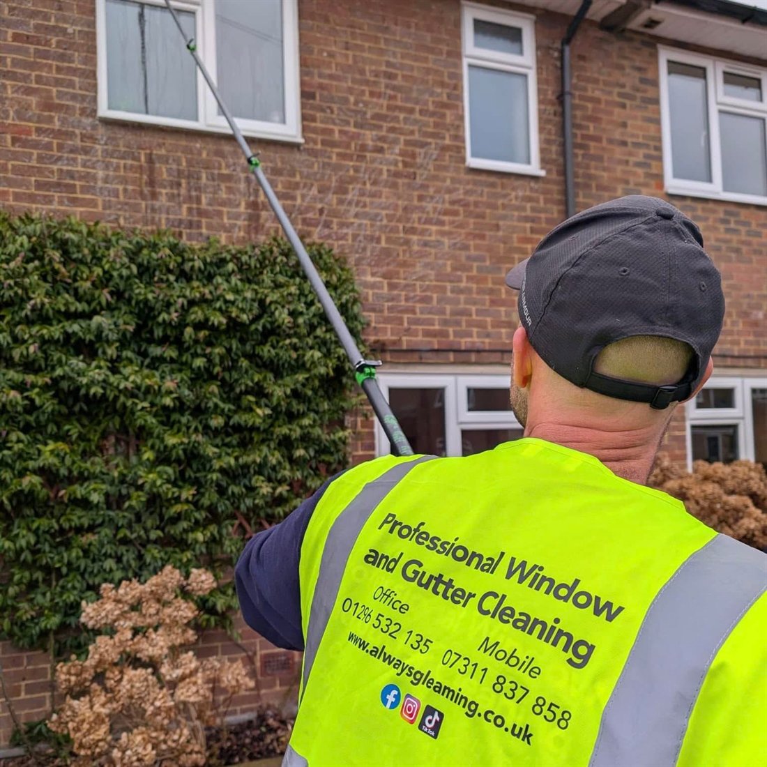 Aaron cleaning first-floor windows with a water-fed pole, wearing an Always Gleaming hi-vis vest